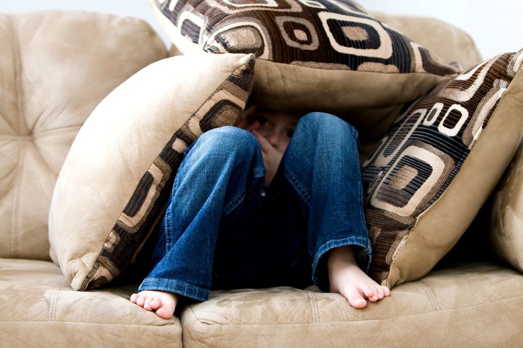 Sacred girl hiding in pillows on sofa